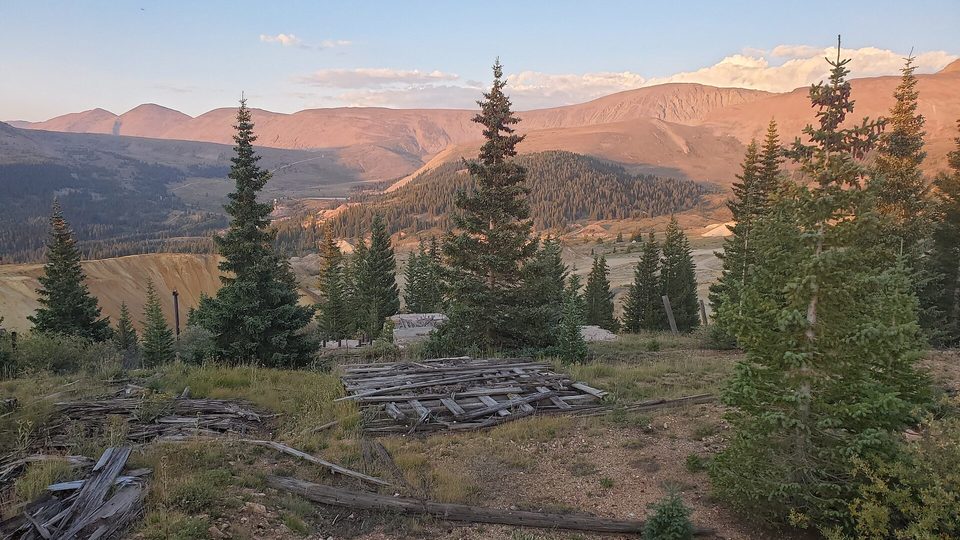 Weathered timbers of the Ibex Mine with bare orange mountains behind at sunset