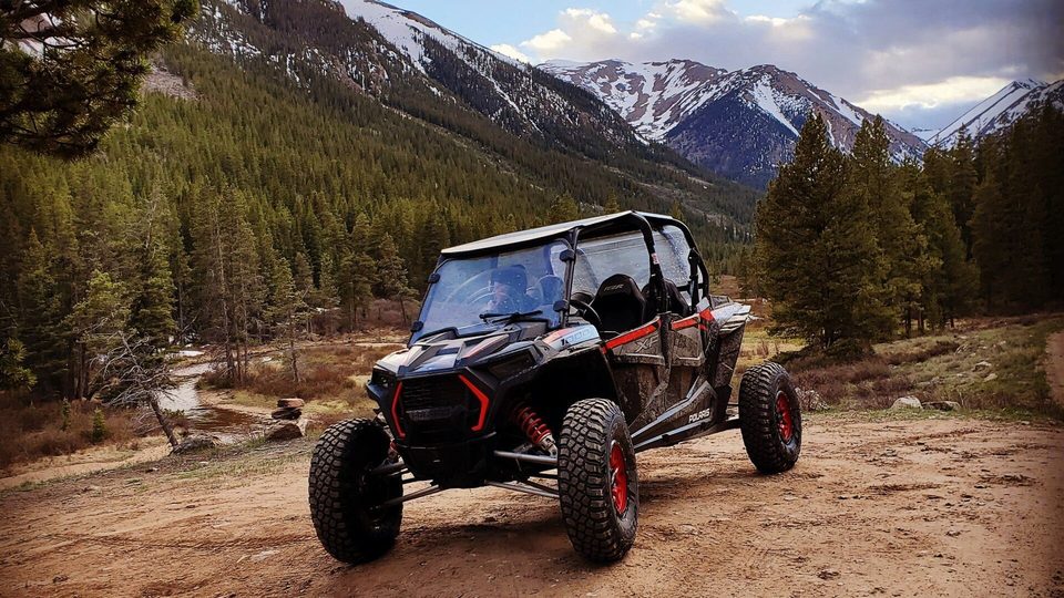 Polaris RZR XP 1000 on a dirt road with a creek and snowy mountains behind