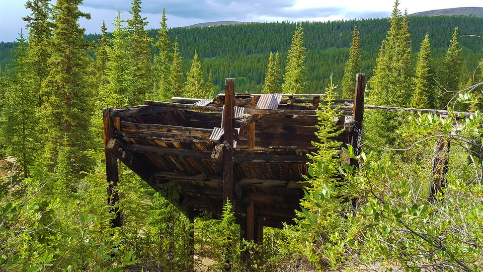 An abandoned wooden ore chute overgrown with green brush