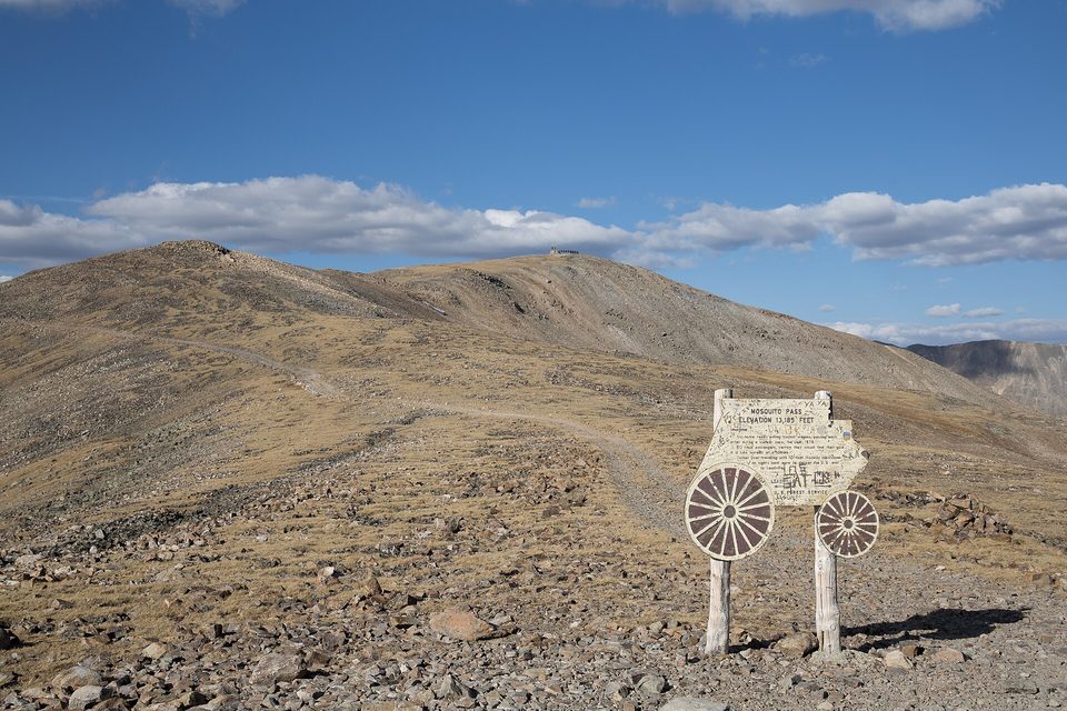 The Mosquito Pass summit sign and a wagon wheel marker at 13,185 feet, bare tundra all around