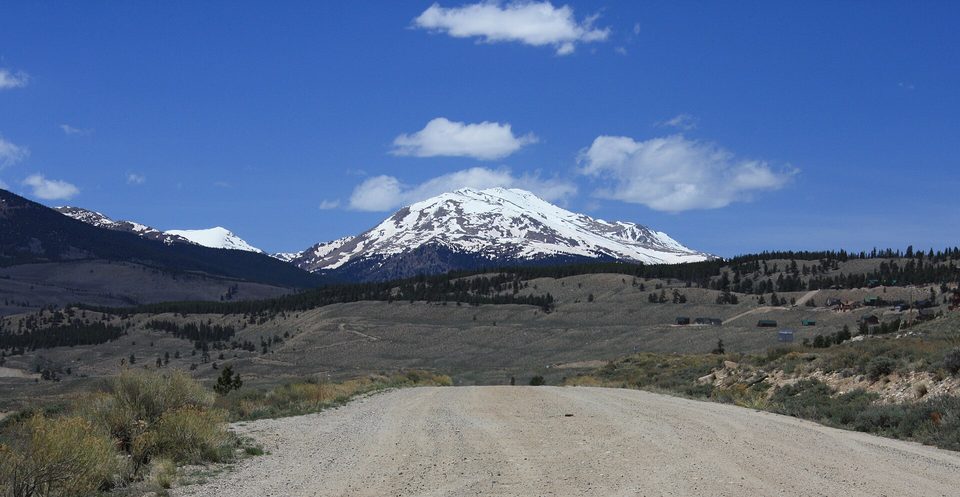A gravel road heading toward snowy Mount Massive under a blue sky