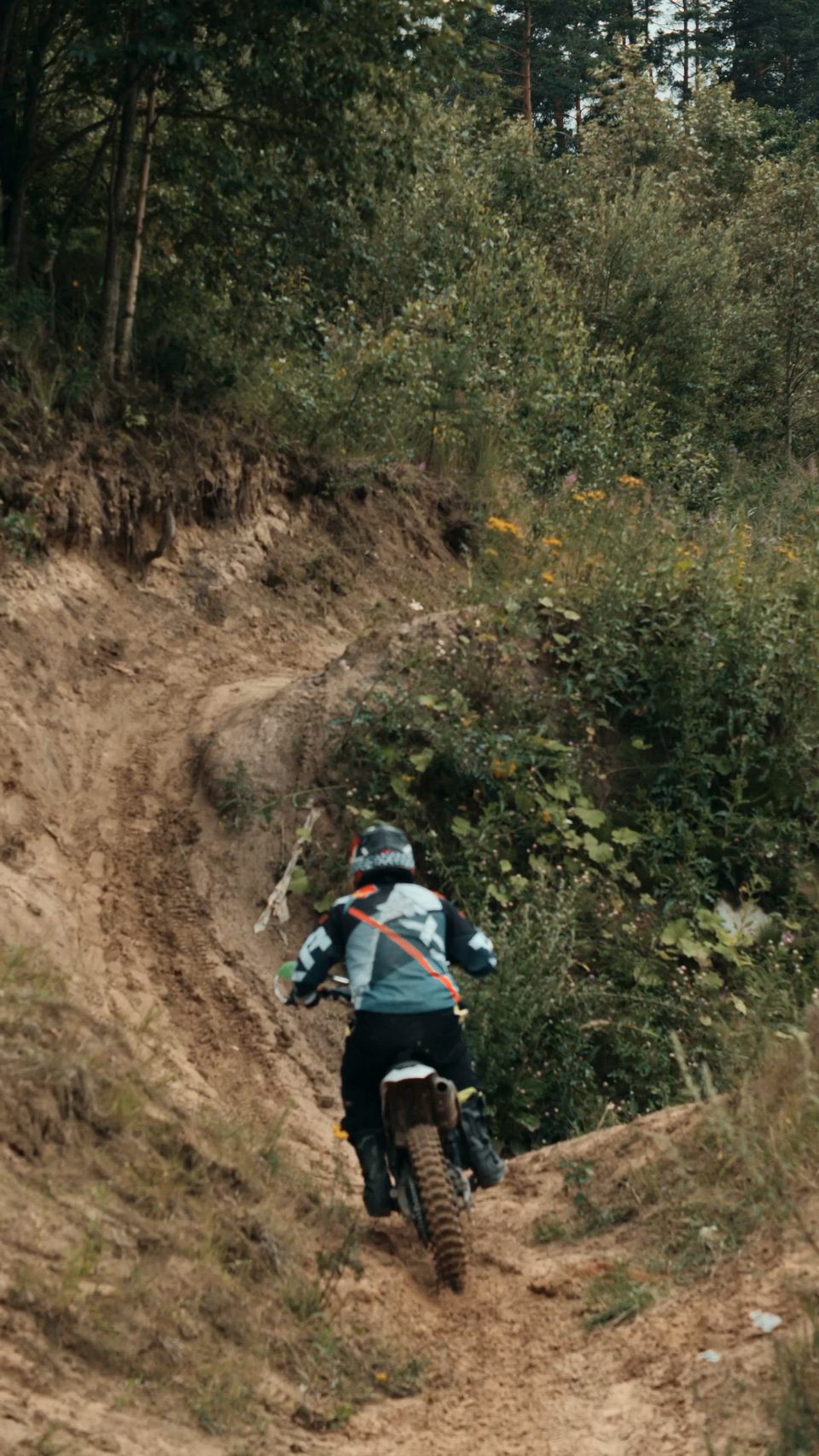 A dirt bike rider climbing a steep dirt hill through brush